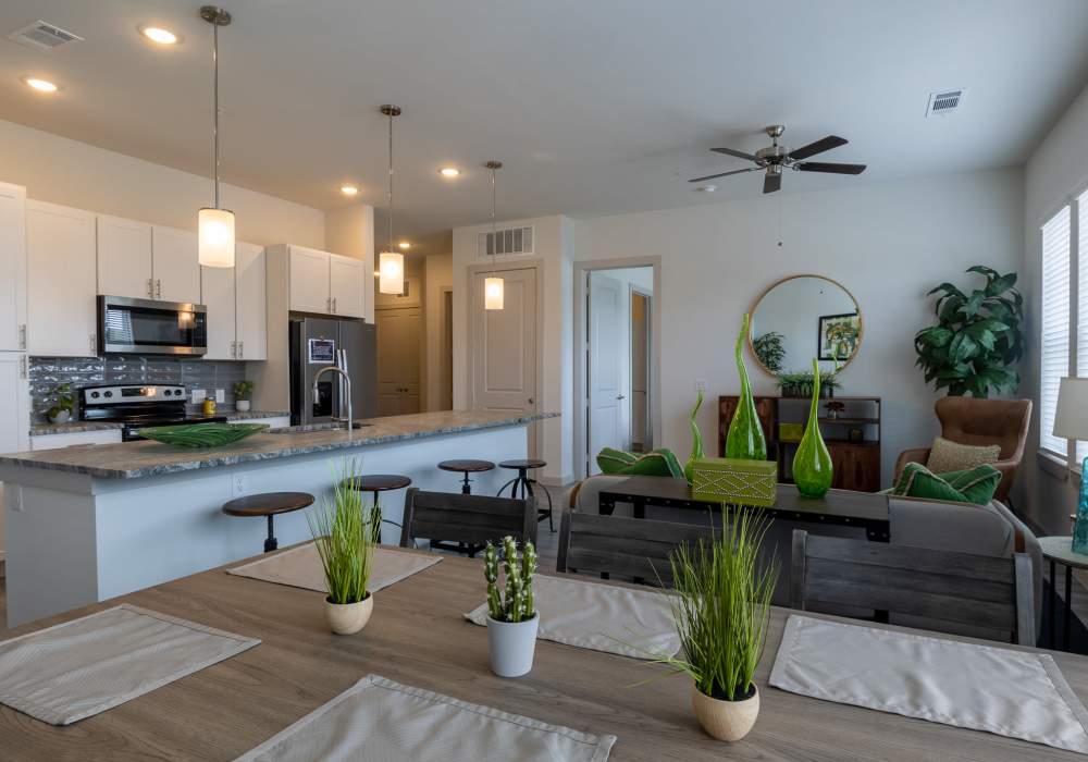 Open-concept apartment living area featuring a dining table with place settings in the foreground at Charleston at Fannin Station in Houston, Texas