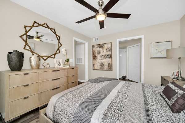 A cozy bedroom featuring a ceiling fan and a wooden dresser against a softly at The Summit At Metrowest in Orlando, Florida