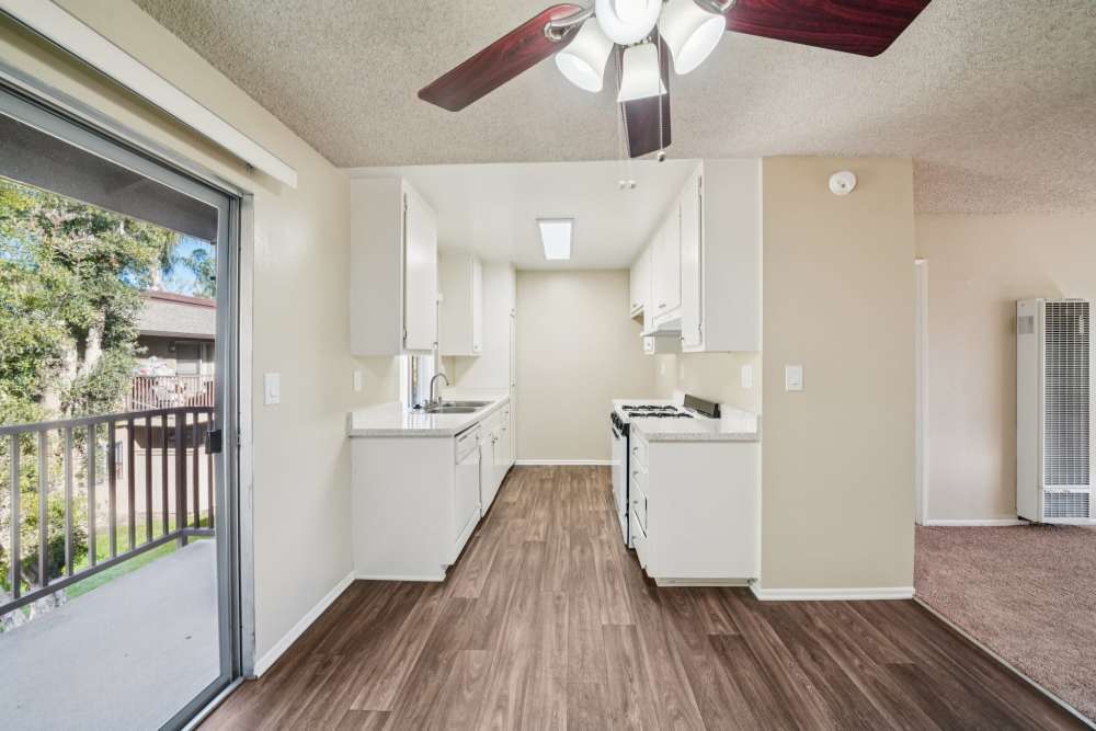 Bright kitchen with white cabinets, wood‑style flooring, and a balcony view at Casa Sierra Apartments in Riverside, California
