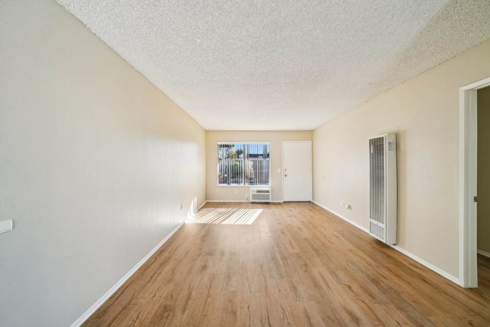 Bright living room with wood‑style flooring and a large window at Casa Sierra Apartments in Riverside, California