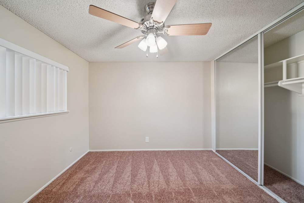 Bedroom with carpet flooring, a ceiling fan, and mirrored closet doors at Casa Sierra Apartments in Riverside, California
