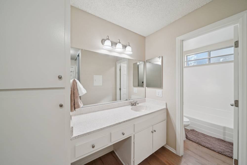 Bathroom with a long vanity, large mirror, and a separate tub and toilet area at Casa Sierra Apartments in Riverside, California