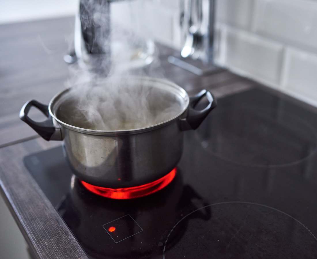 A metal pot with steam rising sits on an active ceramic cooktop, glowing red at Dohr Apartments in Rochester, New York