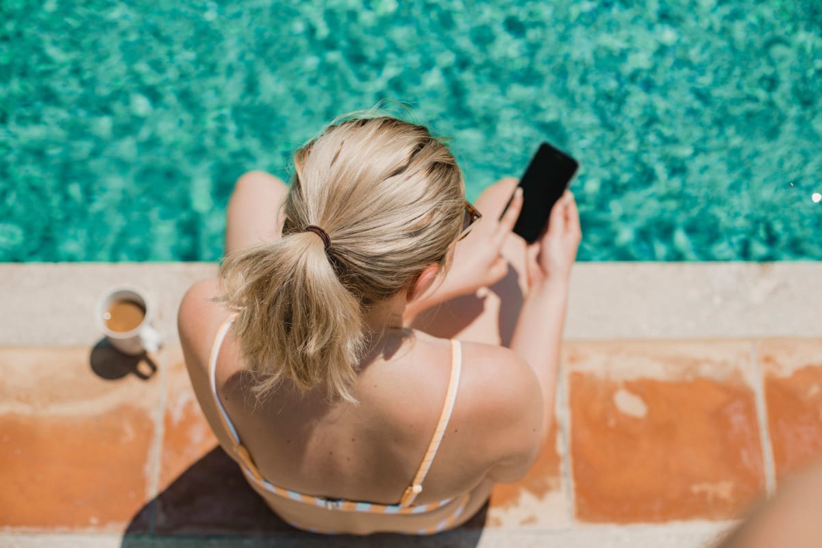 Woman putting her feet in the pool and looking at her phone at Via Holon Apartments in Greenbrae, California