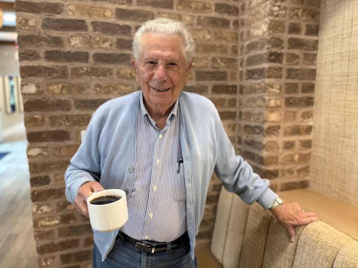 Frank Amato holds a cup of coffee and smiles in the lounge at Clearwater Newport Beach.