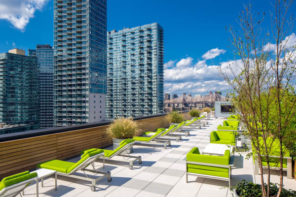 Incredible spacious rooftop patio with lounge chairs and a gorgeous view of the city at The Maximilian in Queens, New York