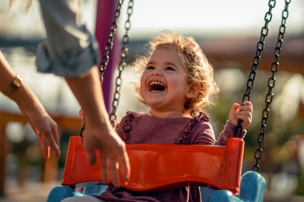 Mom pushing her laughing toddler in a swing at the playground at James River Pointe in Richmond, Virginia