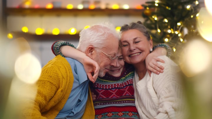Young child hugging grandmother and grandfather near holiday lights and decorations