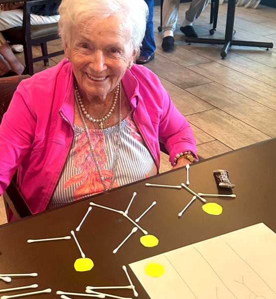 Smiling senior woman engaging in a brain-stimulating activity using cotton swabs and yellow markers to form patterns—part of a cognitive wellness program at Clearwater.