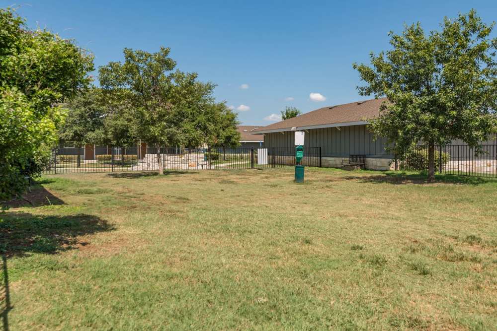 South Austin, TX Luxury Studio Apartments - Landing at Double Creek - Bark Park With Lush Grass, Rest Area, And A Bench Surrounded By Trees.