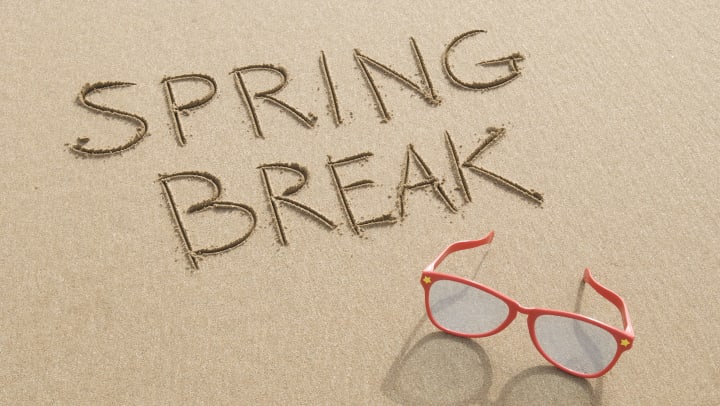 The words “Spring Break” written in the sand with red sunglasses next to it. 