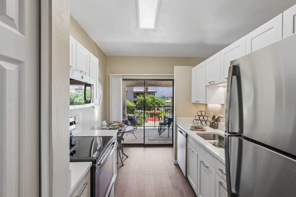 Galley-style kitchen with white cabinetry, stainless steel refrigerator, and wood-look flooring at Oro Vista Apartments in Oro Valley, Arizona