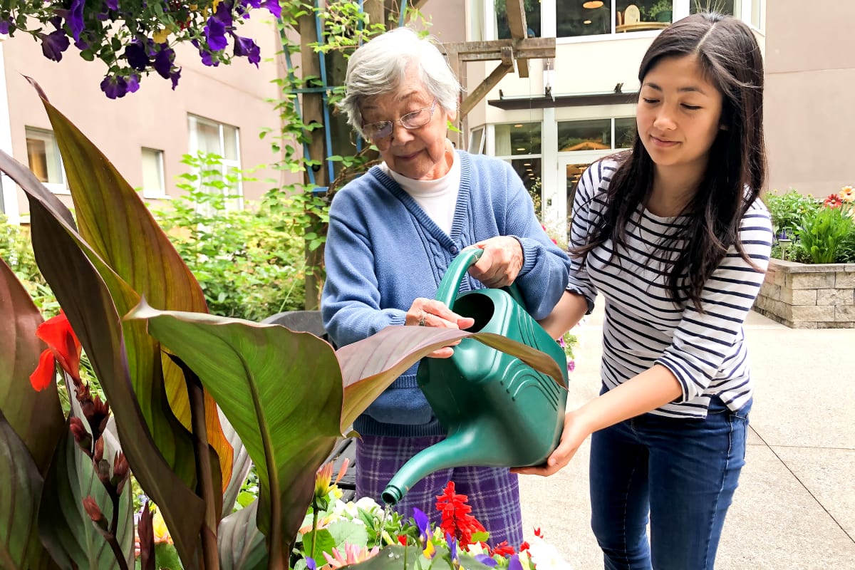 A resident and her granddaughter watering flowers at Claiborne Senior Living.