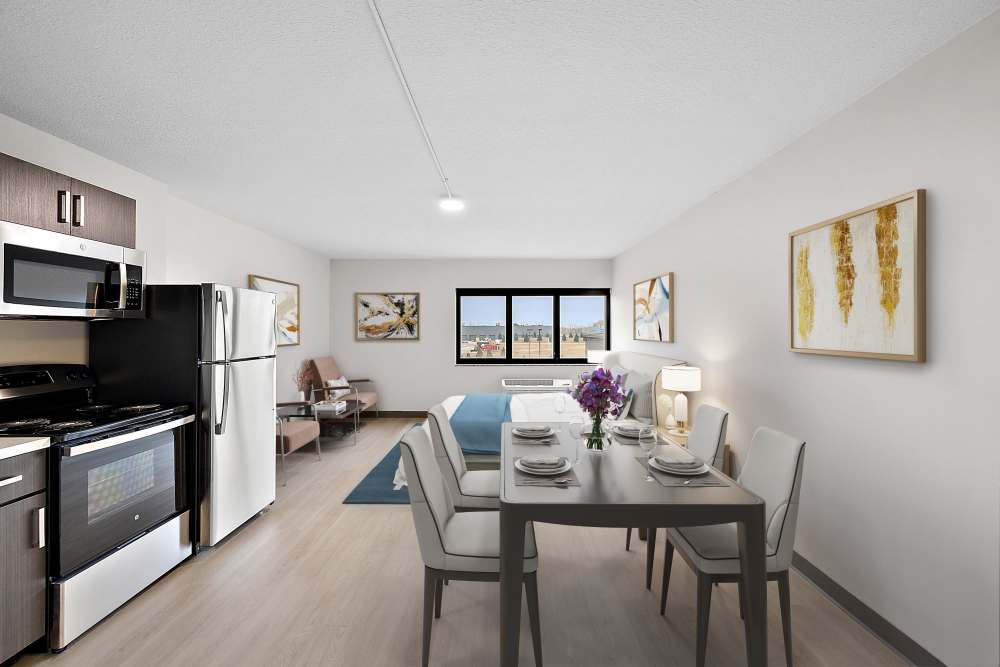 Open-layout kitchen and living room separated by island with waterfall faucet sink and refrigerator at The Block at Sterling Heights in Sterling Heights, Michigan