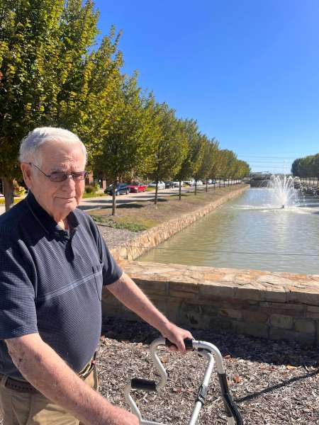 Resident enjoying a sunny stroll by the fountain at The Landing at Watermere Frisco in Frisco, TX, promoting wellness and outdoor engagement.