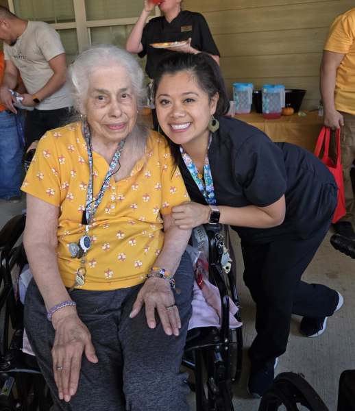 A resident at The Landing at Stone Oak shares a warm moment with a caring staff member during an outdoor community event, highlighting the personalized, compassionate care provided.