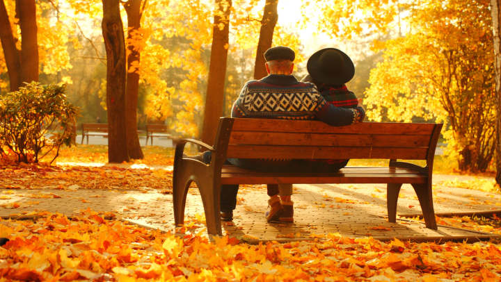 Two seniors sitting on a park bench in fall leaves