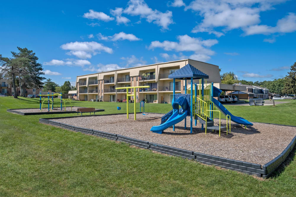 Playground on mulch surrounded by grass with buildings in the background