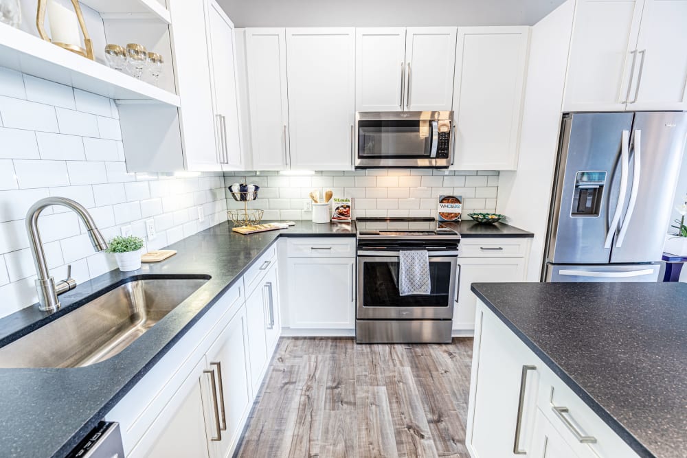 1-Bedroom Apartments in Clayton, MO - The Barton - Gourmet Kitchen with White Tile Backsplash, Dark Countertops, White Cabinets, a Kitchen Island, and Stainless Steel Appliances