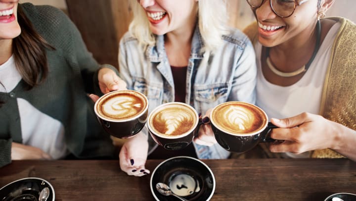 Three women smiling and holding up their coffee cups with foam art.