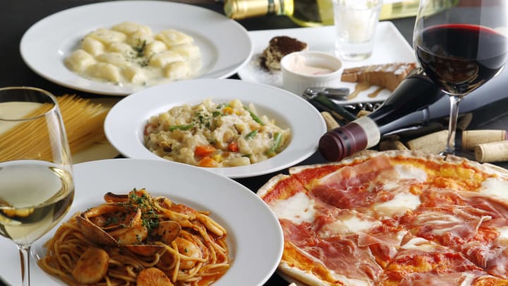 a variety of pizza and pasta dishes on a table with a bottle of wine