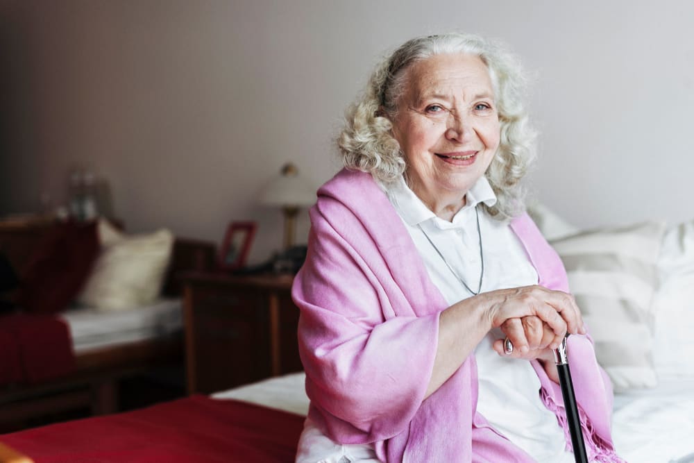 A smiling resident sitting on her bed at Harbor Cove Memory Care in Hilton Head Island, South Carolina