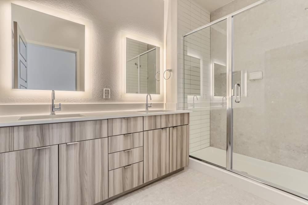Double sink vanity with edge lit mirrors and walk-in shower at Flats on the A in Aurora, Colorado