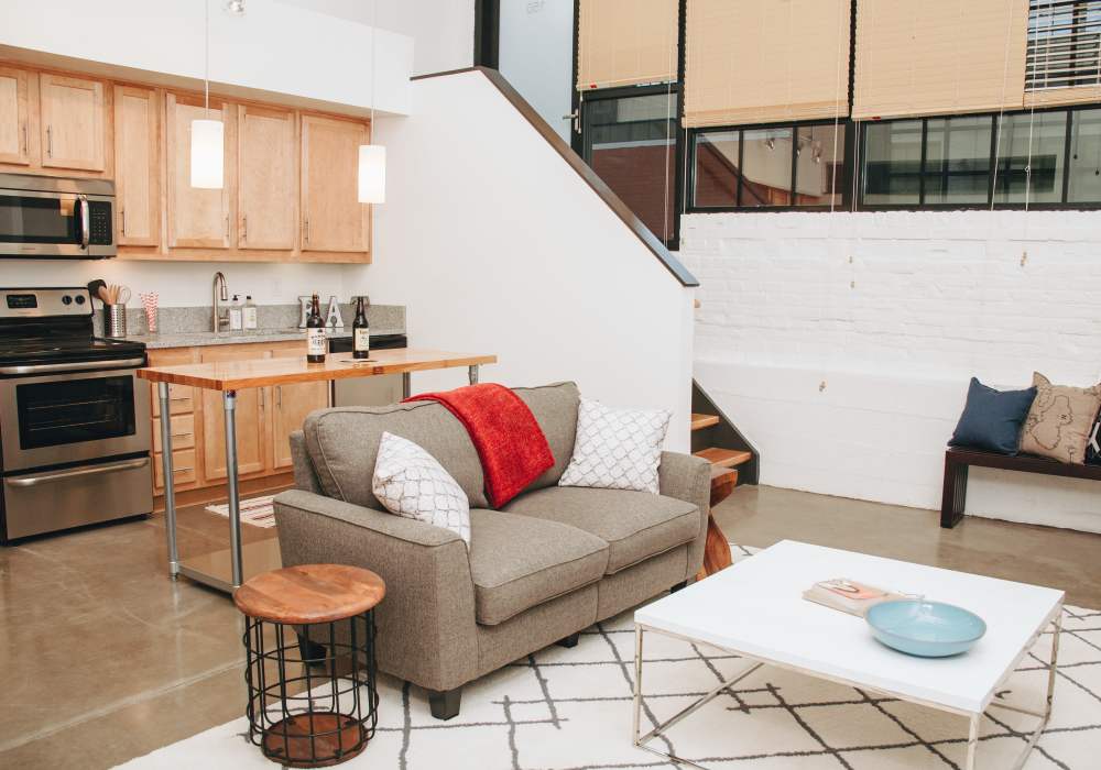 Open layout living room and kitchen with grey sofa, staircase and exposed brick wall at City View Lofts in Richmond, Virginia