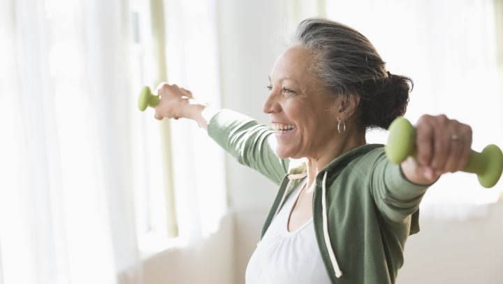 Woman smiling in home while lifting small weights