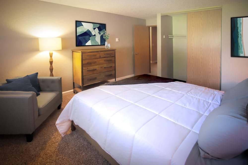 Large bed in carpeted bedroom with sitting chairs at Terra Apartment Homes in Federal Way, Washington