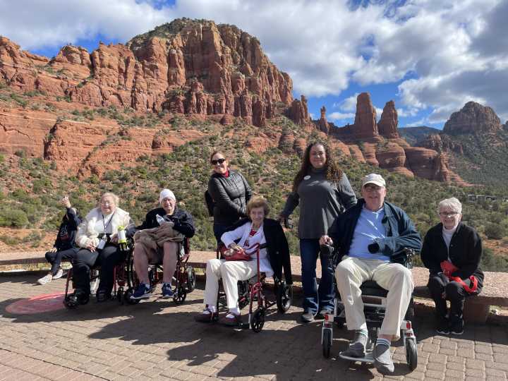 Clearwater residents and team members smiling during an outdoor excursion, seated in front of Sedona’s stunning red rock formations under a partly cloudy sky.