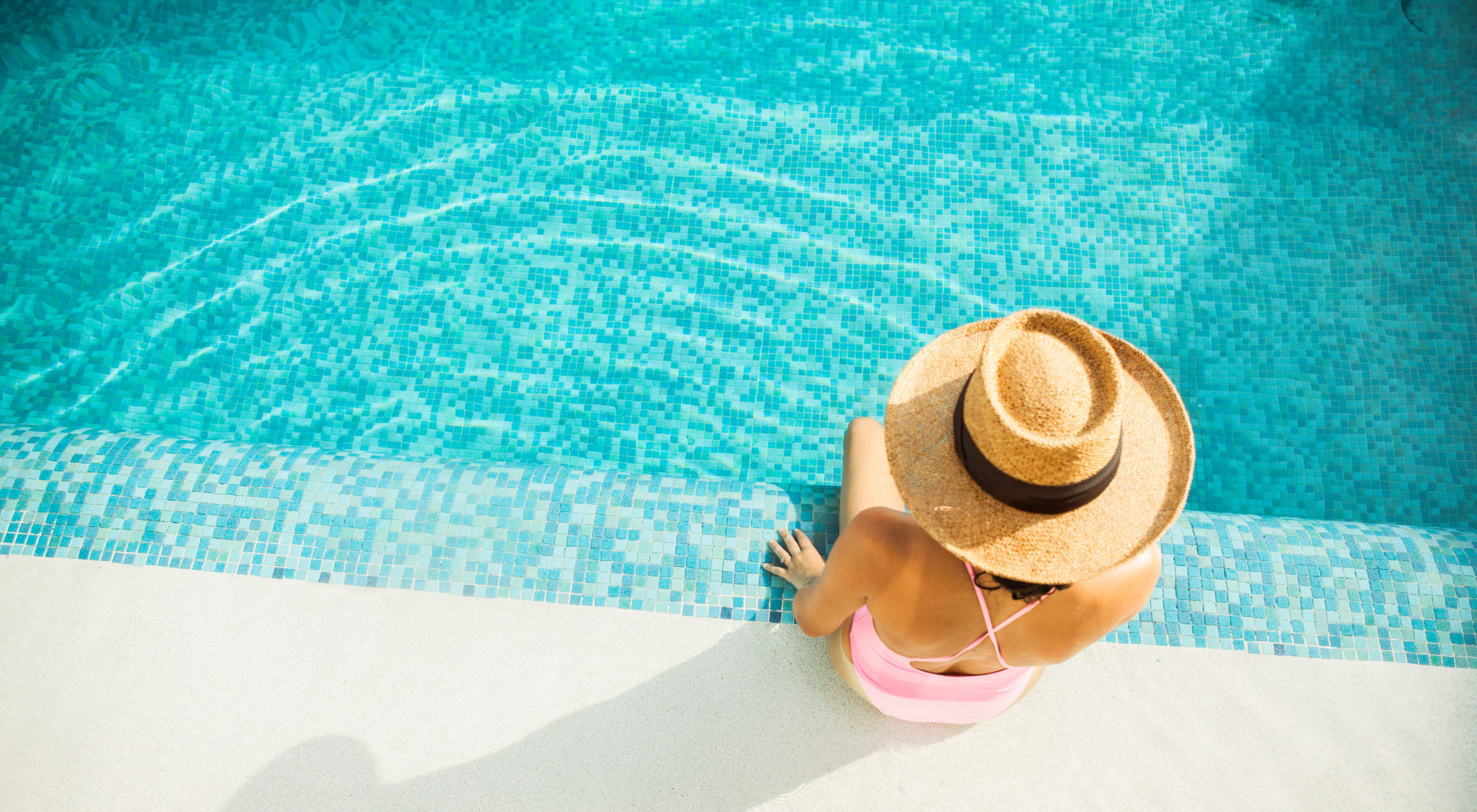 Aerial view of a woman in a wide-brimmed hat sitting by the edge of a pool at Fusion apartments in Jacksonville, Florida