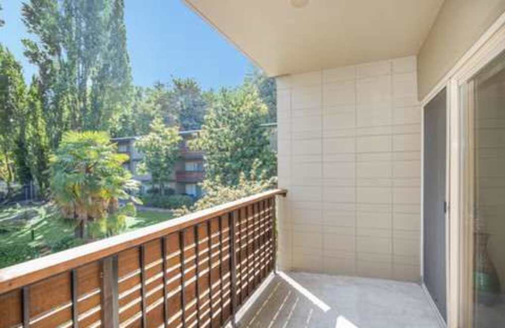 A balcony with a wooden railing overlooking a courtyard with trees atAndanté in Seattle, Washington