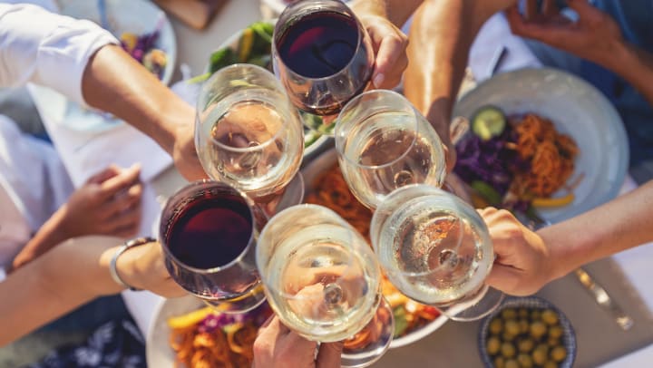 a group of people clinking glasses of red and white wine over a table of food | wineries in Keller
