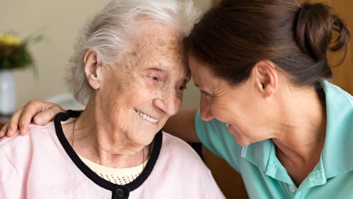 Elderly woman looking at younger woman leaning on each others foreheads. 