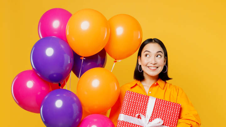 Woman holding a wrapped present and multi-colored balloons