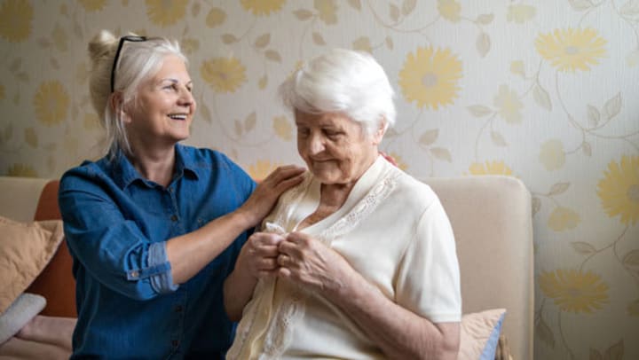 Older woman helping elderly woman get dressed
