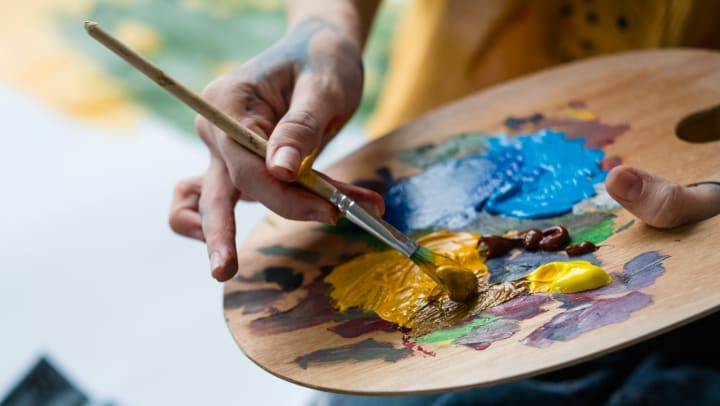 Close-up of artist hands holding wooden palette, mixing acrylic paint with brush