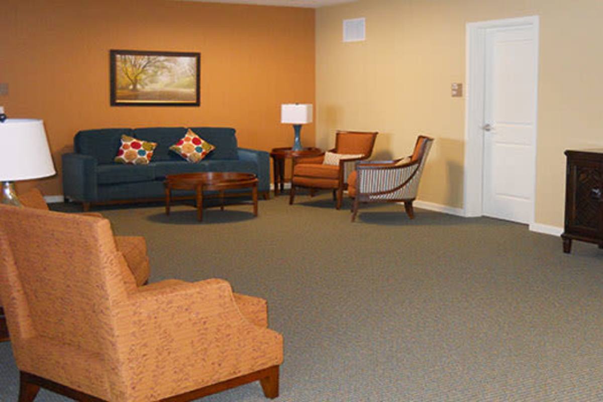 Cozy living area with blue sofa, orange chairs, and wooden coffee table on carpeted flooring at Seton Village Apartments in Emmitsburg, Maryland