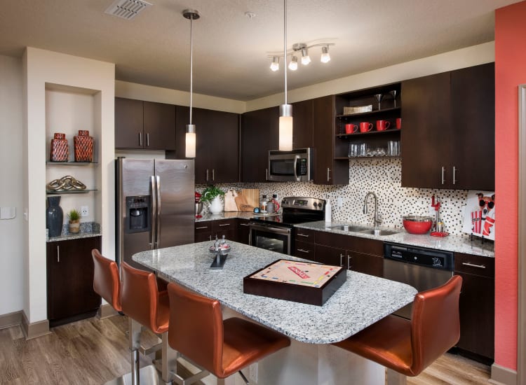Modern kitchen with granite countertops and dark wood cabinetry in a model home at The Courtney at Universal Boulevard in Orlando, Florida