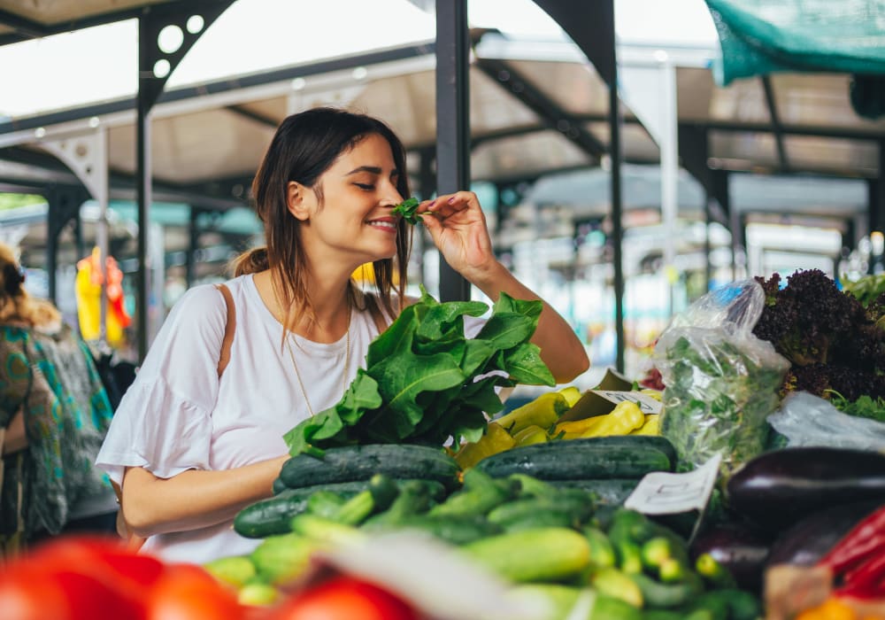 Resident smelling fresh herbs at an open-air farmers market near Skyline Terrace Apartments in Burlingame, California