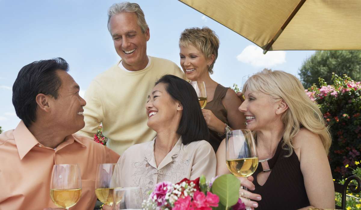 Group of friends enjoying drinks and laughter at a garden table with vibrant flowers at Solera at Avalon Trails in Delray Beach, Florida 