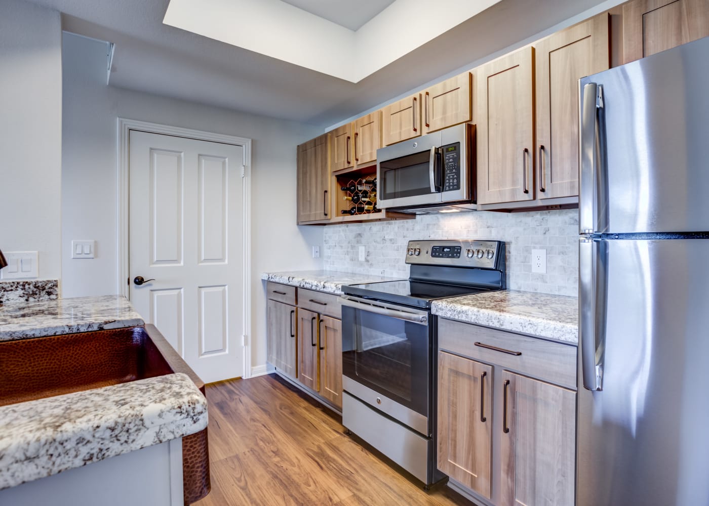 Granite countertops, stainless-steel appliances, and gorgeous wood cabinets and floor in model home kitchen at Riata Austin in Austin, TX