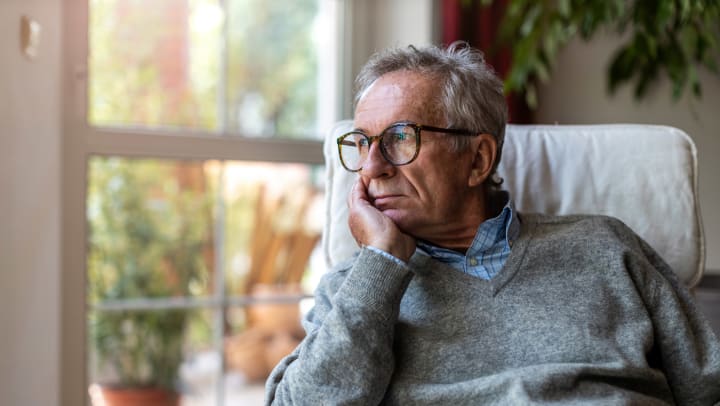 An old man with reading glasses looking at the window