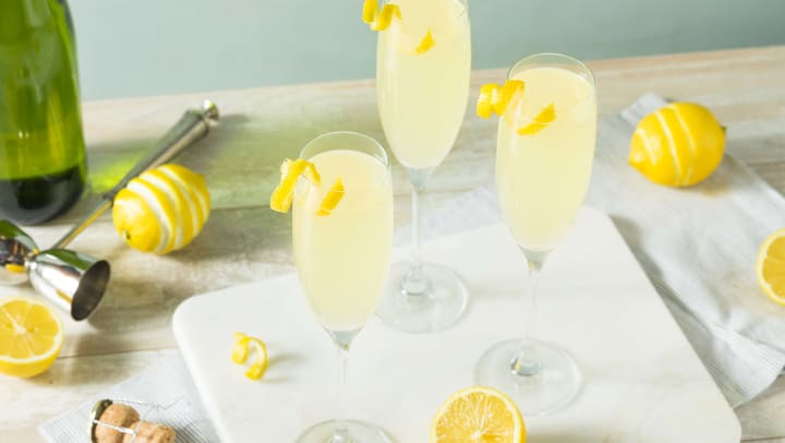 A picture of three champagne glasses on a cutting board with lemons and a bottle of champagne in the background