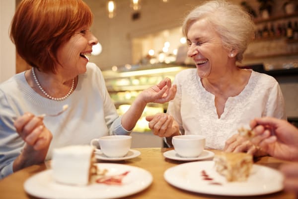 Two senior women laughing over a drink at Clearwater at Riverpark in Oxnard,