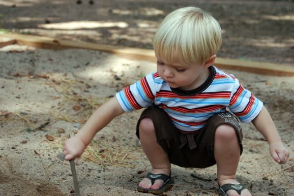 A child playing with a stick in the dirt. 