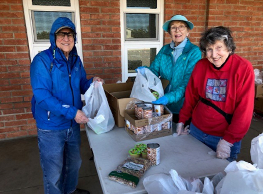 Senior residents volunteering outdoors, smiling as they sort and pack canned goods and pantry items for donation.