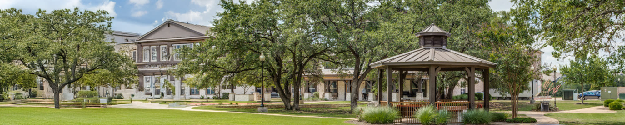 Gazebo surrounded by trees and grass at Isle at Cedar Ridge in Cedar Park, Texas, with the community in view.