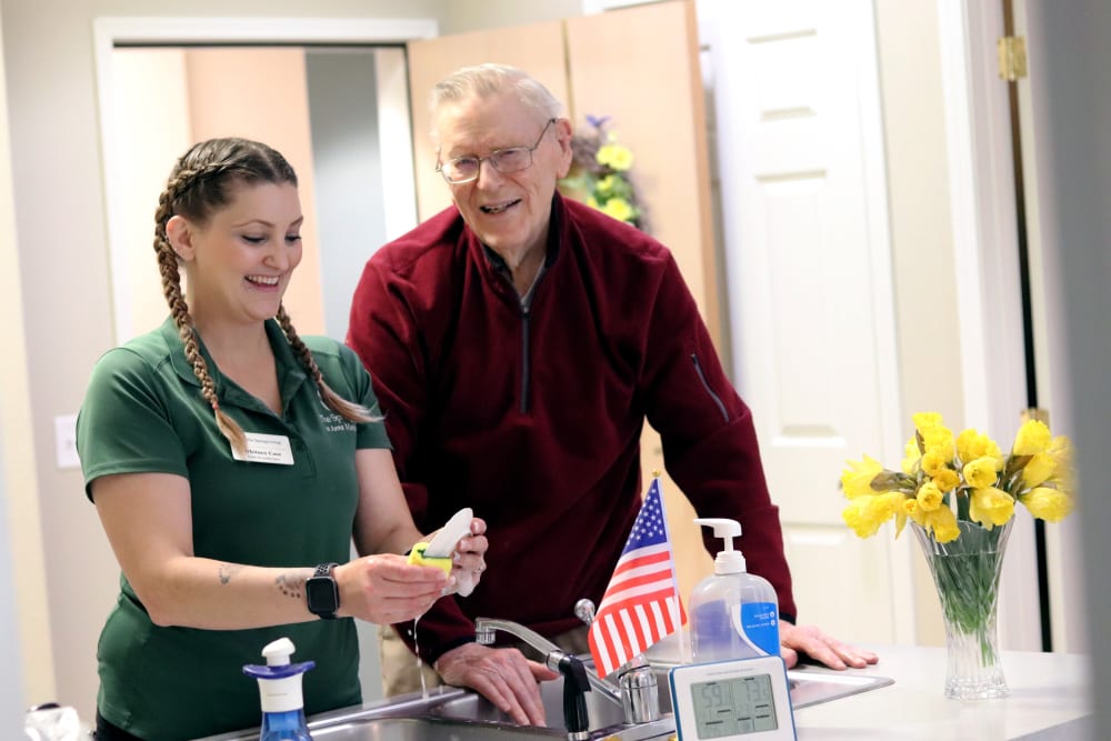 Smiling resident chatting with caregiver as she washes dishes at The Springs at Anna Maria in Medford, Oregon